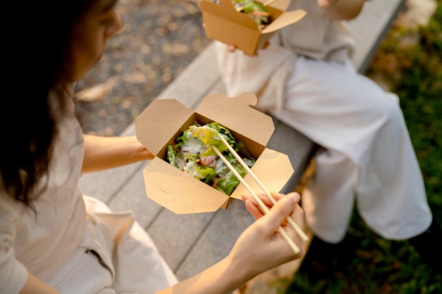 An image of a woman eating a salad out of a cardboard takeout container