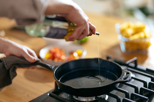 An image of a person pouring oil into a cast-iron skillet