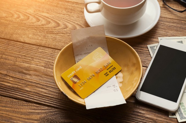 An image of a credit card and a receipt in a dish next to phone and mug
