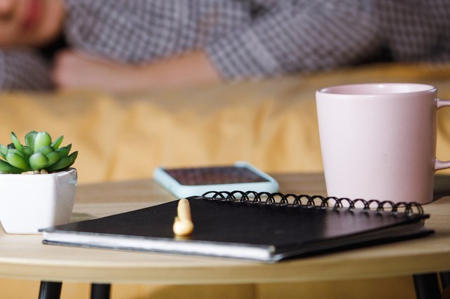 An image of a notebook, coffee mug, phone, and small succulent plant on a nightstand