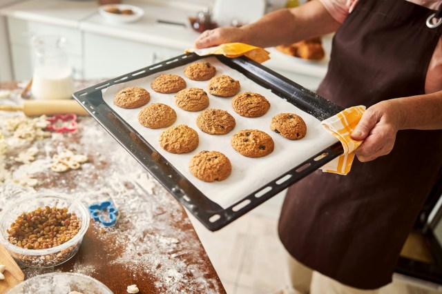 An image of a baker holding a pan of cookies