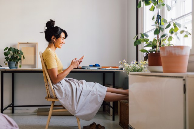 An image of a woman holding her phone while sitting on a wooden chair