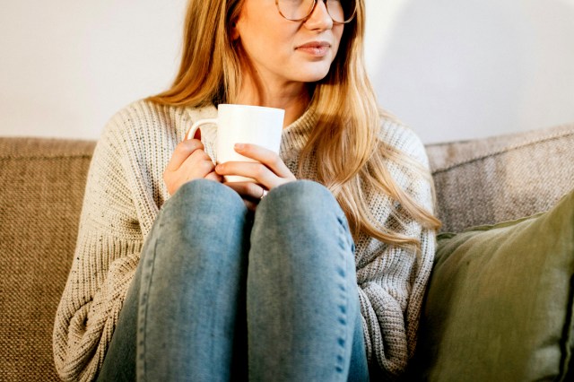 An image of a woman holding a mug and sitting on a couch
