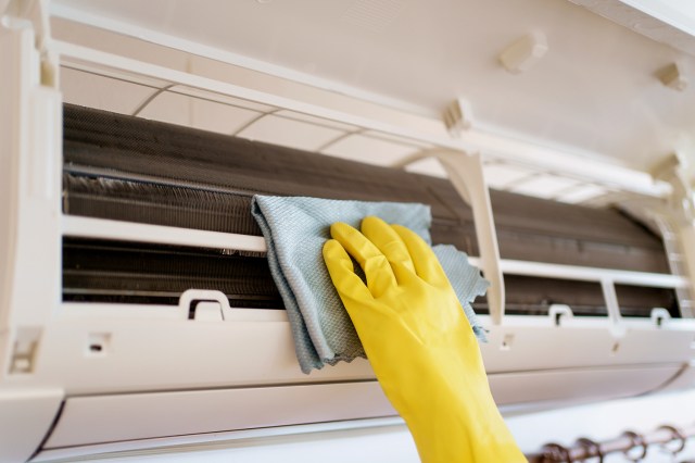 An image of a hand wearing a yellow rubber glove cleaning an air conditioning unit