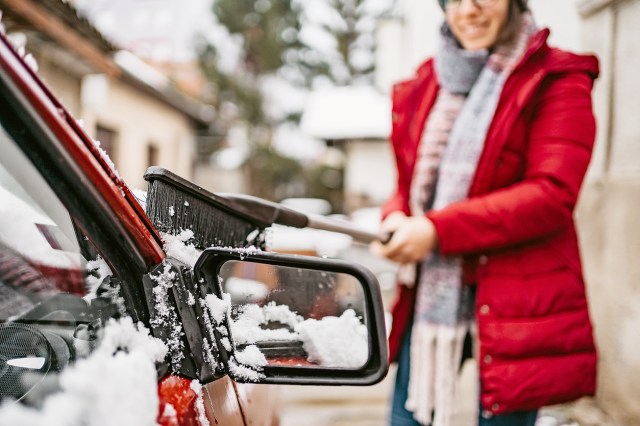 An image of woman brushing snow off a car