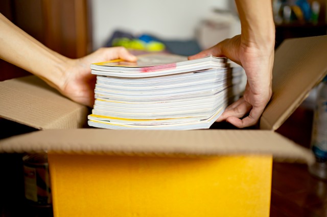 An image of person putting a stack of magazines in a box