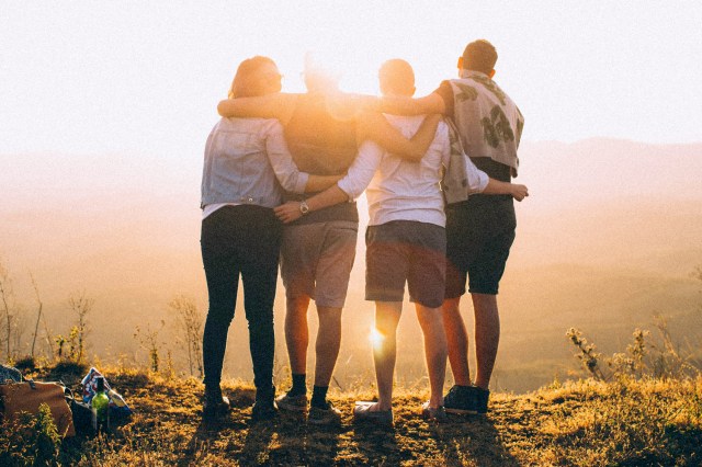 An image of four people looking at the sunset with their arms around each other