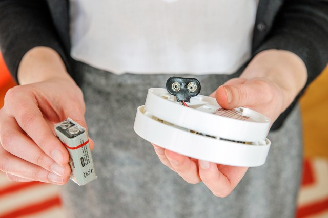 An image of a person holding a smoke detector and a battery