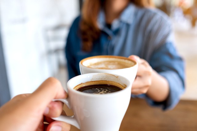 An image of two people toasting with mugs of coffee
