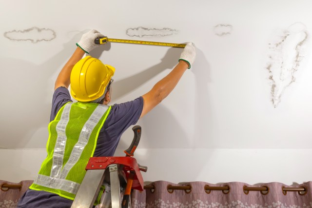 An image of a worker measuring a water stain on the ceiling