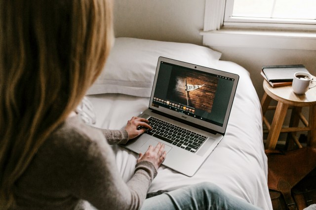 An image of a woman sitting on a bed while on the computer