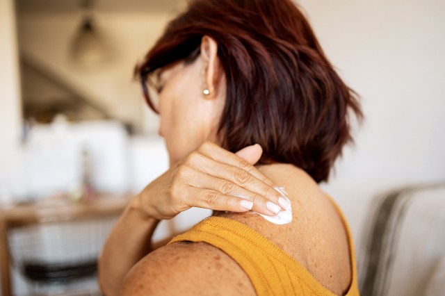 An image of a woman rubbing lotion on her shoulder