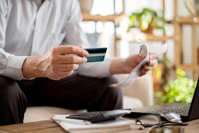 An image of a man holding a credit card and a bill in front of a laptop