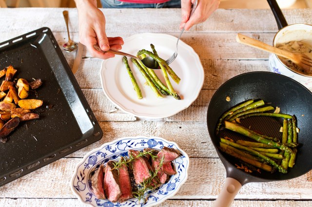 An image of a table with plates of asparagus, steak, and potatoes