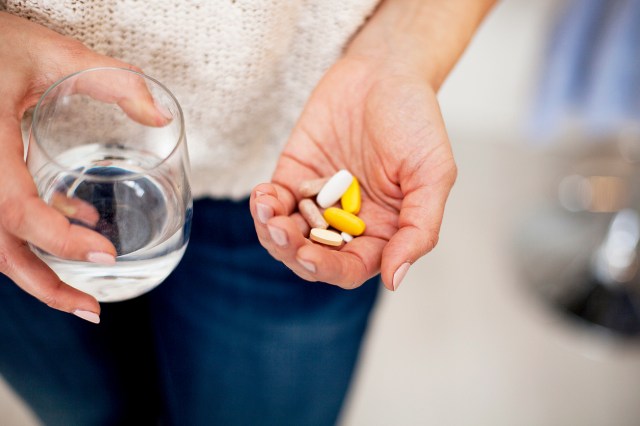 An image of a person holding a glass of water in one hand and pills in the other