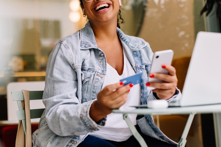 An image of a woman laughing while holding her phone and a credit card