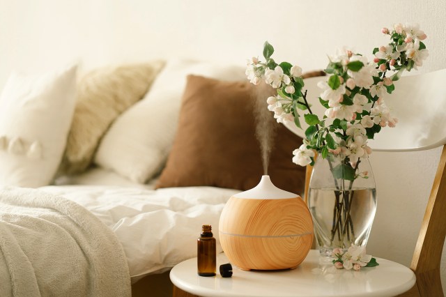 An image of a nightstand with a diffuser and vase of flowers