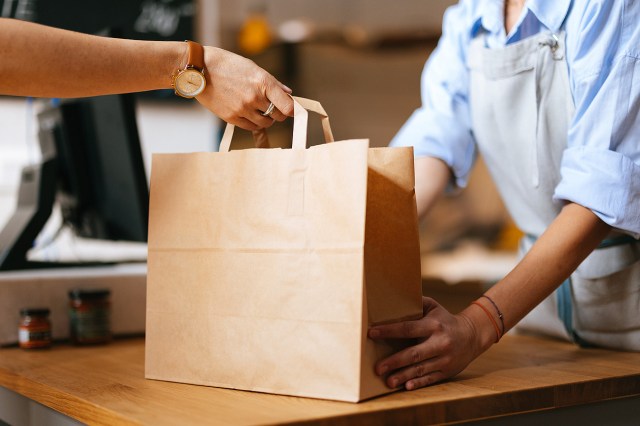 An image of a person grabbing a paper bag from a grocery store worker