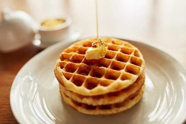 An image of syrup being poured on a stack of waffles