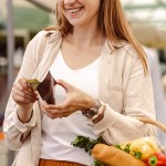 Woman shopping with basket of fruit and vegetables while looking at wallet