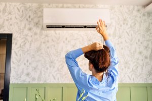 Woman standing before air conditioning unit with her hand up and holding her hair