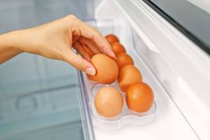Person picking up an egg out of a drawer in the fridge