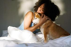 Woman snuggling with small dog on bed