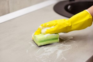 Person scrubbing sink with a green sponge