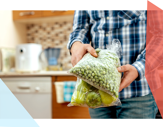 A person holds two clear plastic bags full of frozen vegetables 