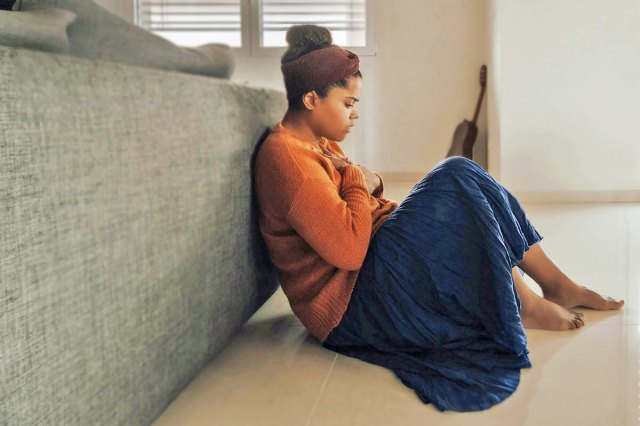 Woman sitting with her back to the back of a couch hunched over