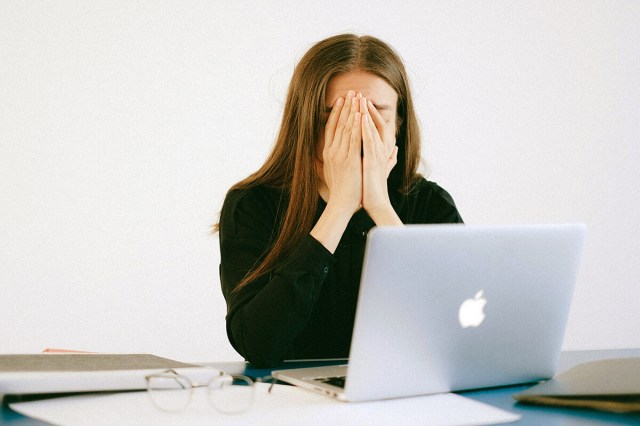 Woman sitting in front of laptop with her hands over her face