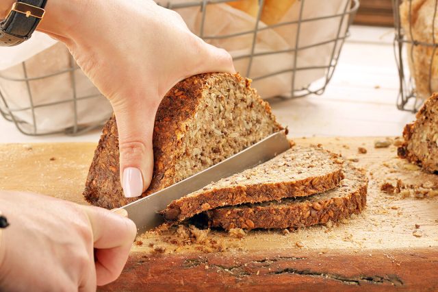 Person slicing loaf of whole grain bread