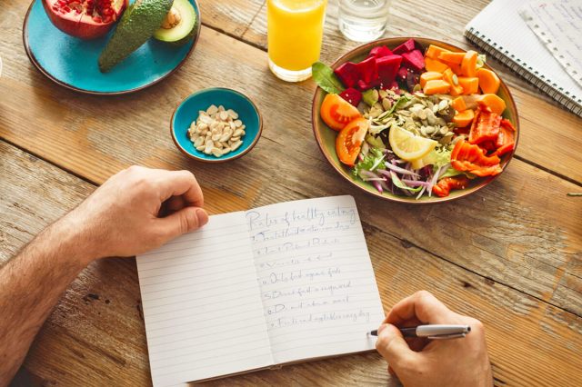 Man writing notes in a notebook with a salad next to him