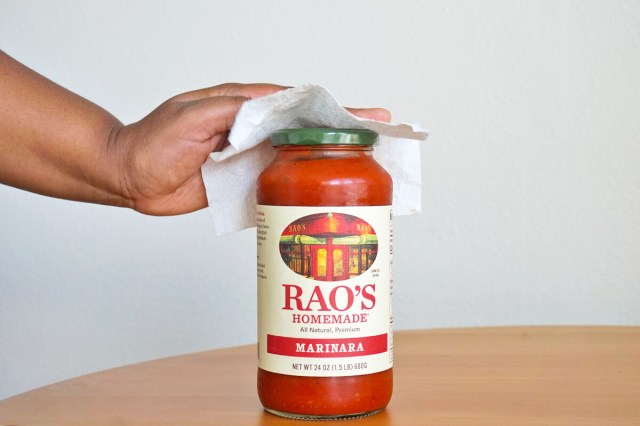 Person wiping down the lid of a jar of marinara sauce