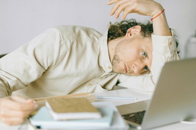 Man hunched over in front of computer with his head on his arm