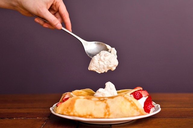 Spoon with whipped cream on it, falling onto a fluffy pancake