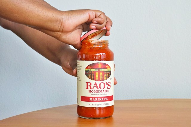 Person using a rubber band around the lid of a jar of marinara sauce to remove the lid