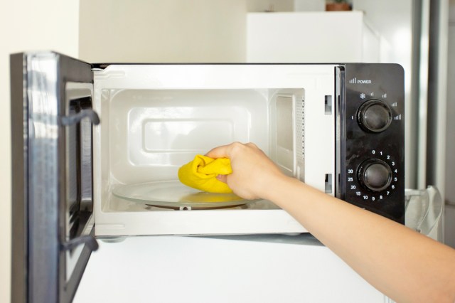 Person wiping down the inside of a microwave with a yellow rag