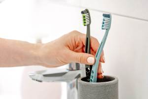 Person putting two toothbrushes in a cup