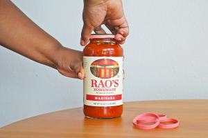 Person putting rubber band around jar of Rao's Homemade Marinara sauce