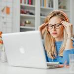 Woman sitting in front of laptop with her hands on her temples