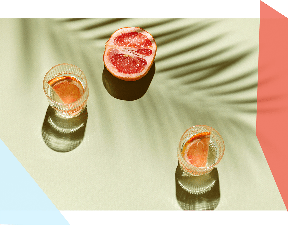 Two glasses with beverages in them next to a piece of fruit 