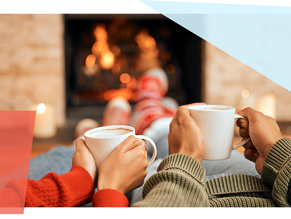 Two people holding coffee mugs near a fireplace 