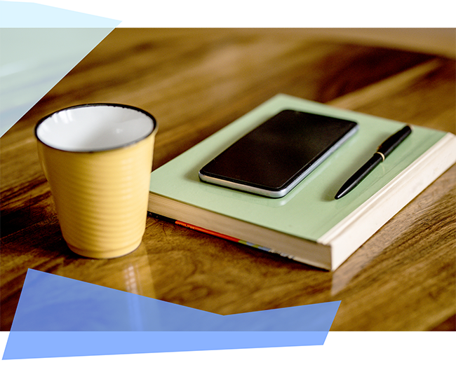 Phone on a stack of notebooks next to a cup 