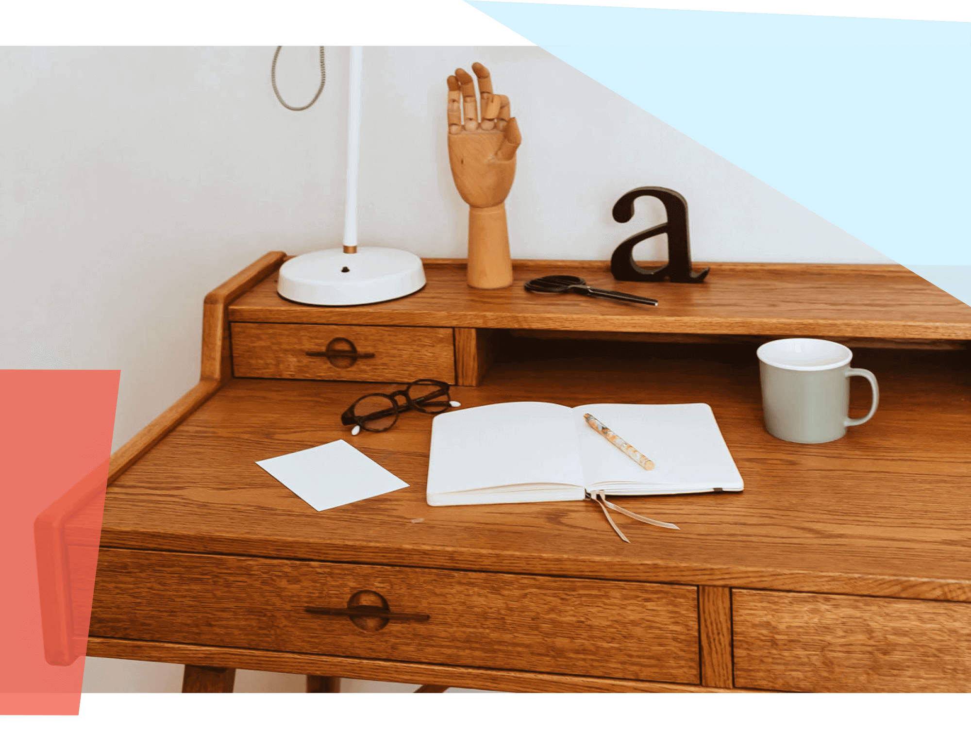 An open notebook and pen sitting on a desk, surrounded by a coffee mug, glasses, lamp and other desk accessories 