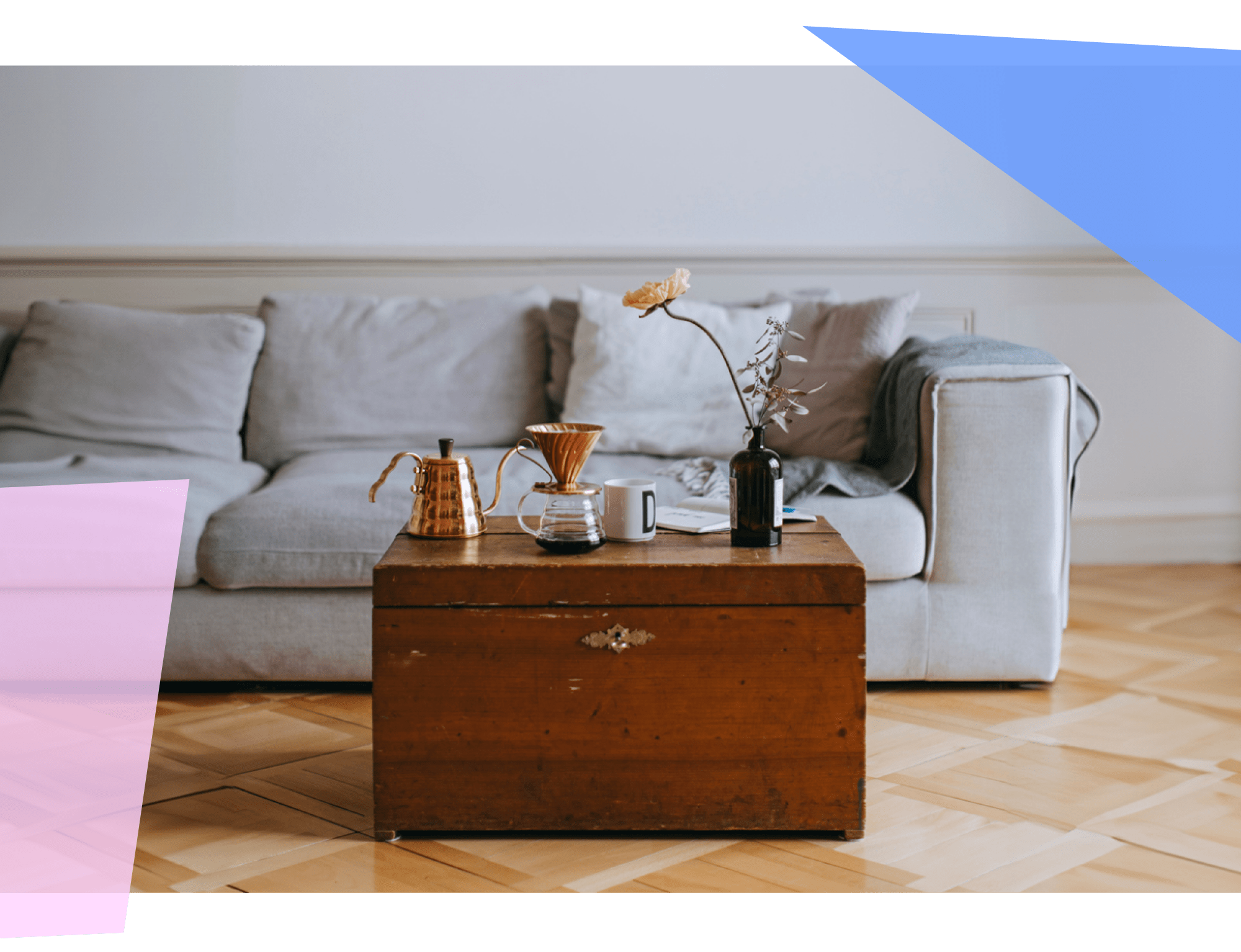 A wooden chest with pour over coffee and a flower on top of it, in front of a couch 