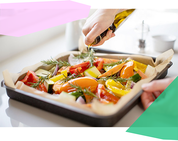 Person drizzling olive oil over a sheet pan of veggies. 