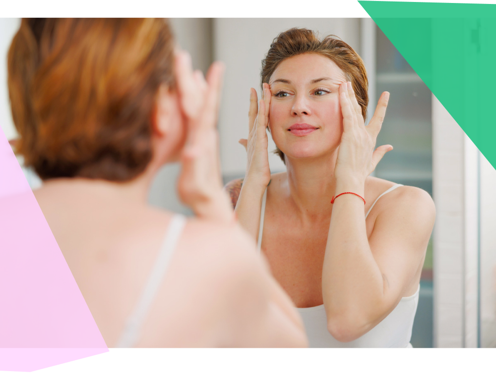 Adult woman massaging face around eyes in front of bathroom mirror