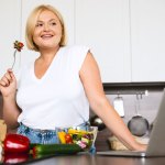 Woman in kitchen eating fruit, with a strawberry on a fork