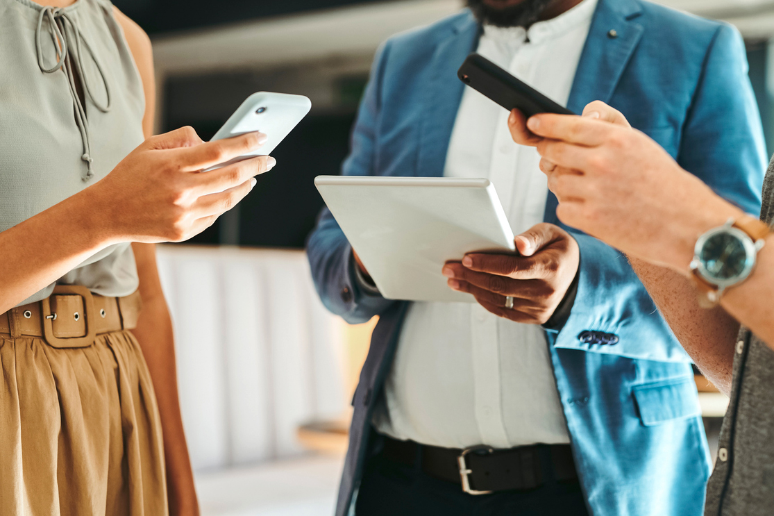 Group of people standing in circle looking at phones and tablets 